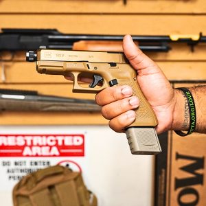 FDE Mag extension for 17 round magazine for Glock in tan pistol in hand facing left